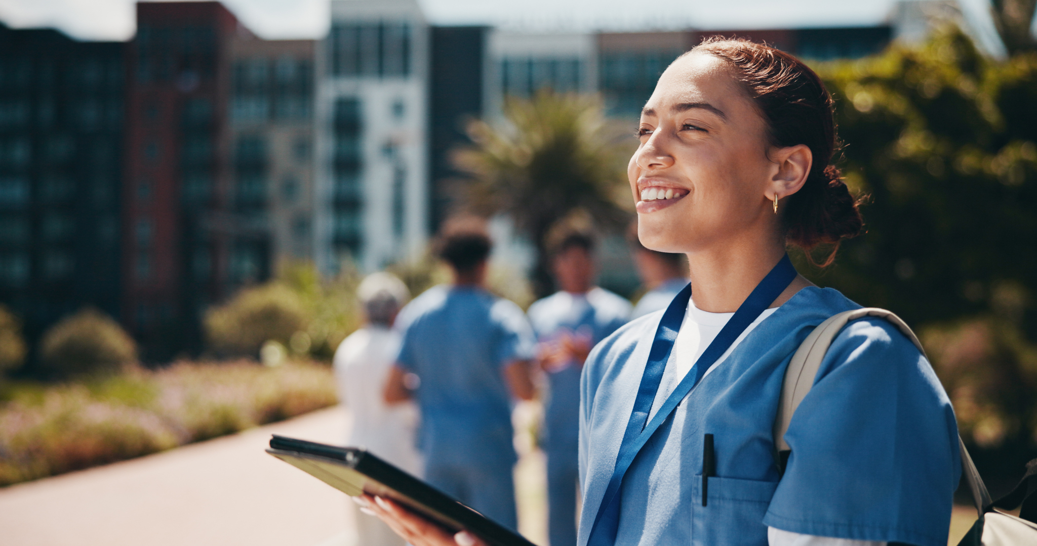 Smiling healthcare student in scrubs holding a tablet outdoors